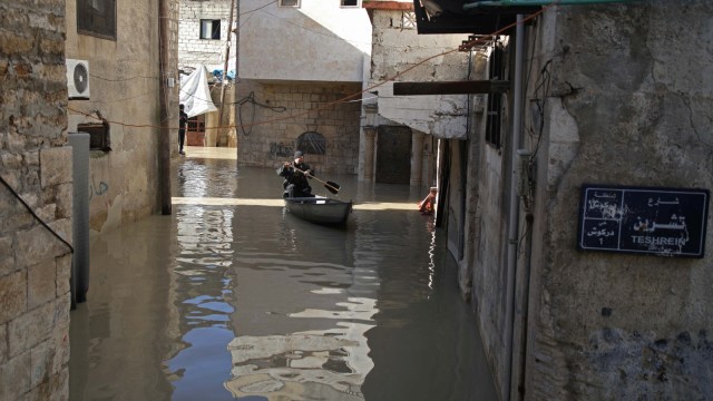 Abu Ihab mengayuh perahu kecil di sepanjang jalan yang banjir di kota Darkush. (Foto: AFP/Aaref WATAD)
