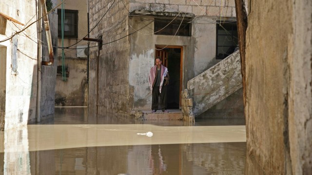 Seorang pria berdiri di pintu depan rumahnya memandang ke jalan yang banjir di kota Darkush. (Foto: AFP/Aaref WATAD)