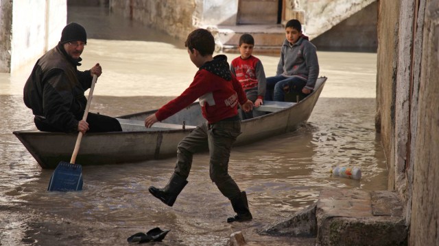 Seorang anak menunggu untuk naik ke perahu kecil di sepanjang jalan banjir di kota Darkush. (Foto: AFP/Aaref WATAD)