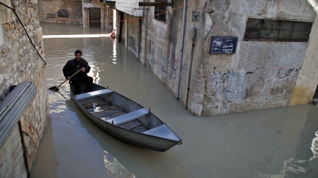 Seorang pria mengayuh sebuah perahu kecil di sepanjang jalan yang banjir di kota Darkush. (Foto: AFP/Aaref WATAD)