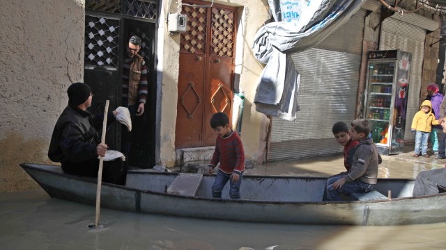 Abu Ihab mengangkut anak-anak dan mengantarkan roti dayung sebuah perahu kecil di sepanjang jalan yang banjir di kota Darkush (Foto: AFP/Aaref WATAD)