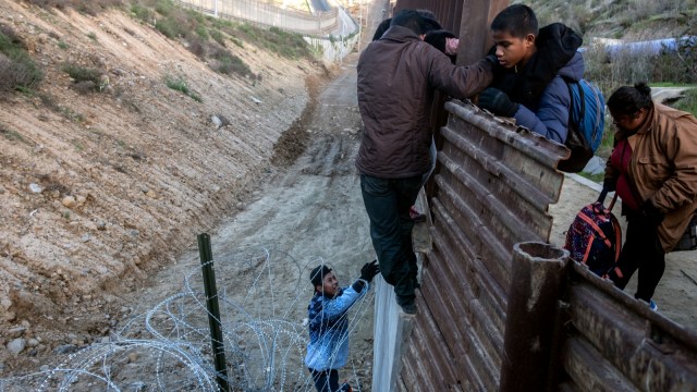 Imigran Amerika Tengah melintasi pagar perbatasan AS-Meksiko dari Tijuana ke San Diego County. Foto: AFP/GUILLERMO ARIAS