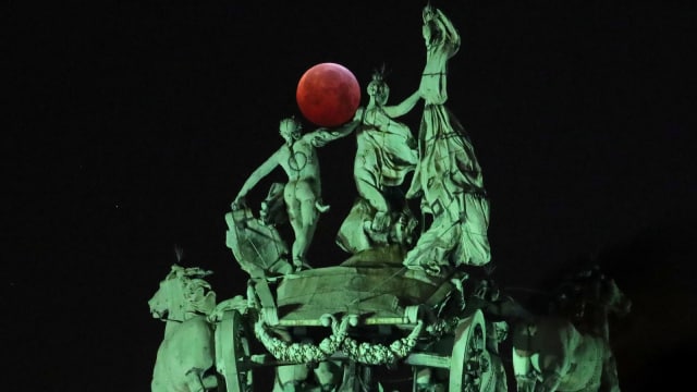 Fenomena 'super blood wolf moon' terlihat di dekat sebuah patung selama gerhana bulan di Brussels, Belgia,(21/1). (Foto: REUTERS / Yves Herman)