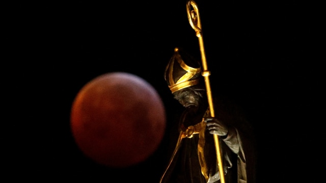 Fenomena 'super blood wolf moon' terlihat di dekat sebuah patung selama gerhana bulan di Grand Place Brussels, Belgia, (21/1). (Foto: REUTERS / Francois Lenoir)