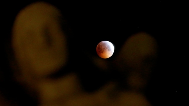 Fenomena 'super blood wolf moon' terlihat di dekat patung selama gerhana bulan total di Marseille, Prancis, (21/1).  (Foto: REUTERS / Jean-Paul Pelissier)