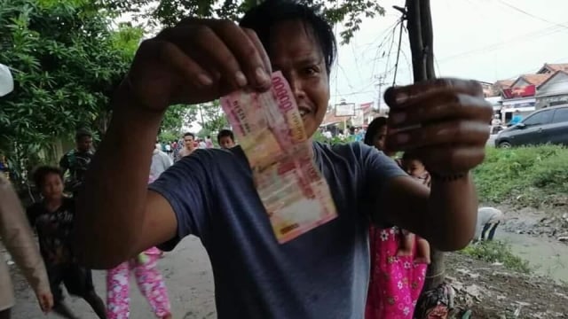 Salah seorang warga memperlihatkan uang yang berhasil di temukannya dari dalam  sungai (Foto: Facebook/ Yuni Rusmini)