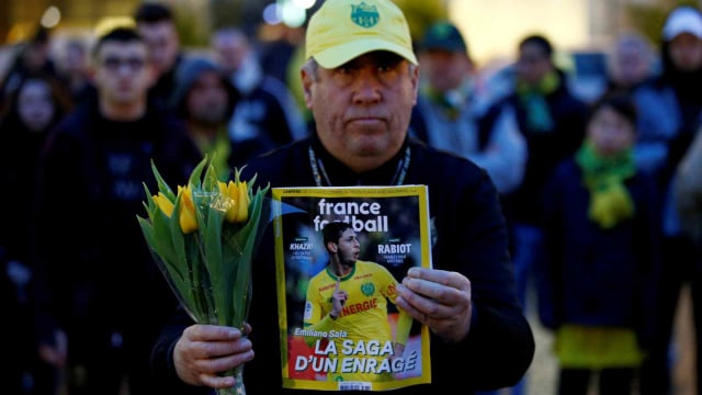 Seorang pria memegang majalah olahraga yang bergambar Emiliano Sala dan memegang bunga tulip kuning di pusat kota Nantes untuk menghormati dan memberikan dukungan terhadai penyerang idola mereka, Emiliano Sala. (Foto: REUTERS/Stephane Mahe)