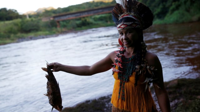 Seorang wanita Pribumi dari suku Pataxo Ha-ha-hae membawa ikan mati di dekat sungai Paraopeba. (Foto: REUTERS/Adriano Machado)