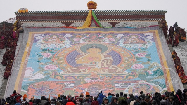 Biksu-biksu di Tibet membentangkan thangka raksasa, lukisan sutra religius yang memajang potret Buddha, di tengah hujan salju di Langmu Lamasery, Prefektur Otonomi Tibet Gannan, Provinsi Gansu, Cina. Foto: REUTERS/Aly Song