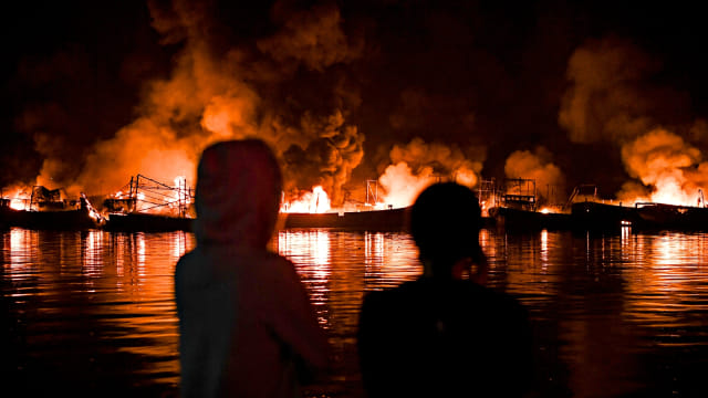 Warga melihat kapal-kapal nelayan yang terbakar di Pelabuhan Muara Baru, Jakarta. Foto: Antara/Hafidz Mubarak 