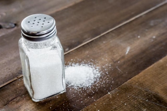 Botol garam dan tumpahan garam di meja kayu