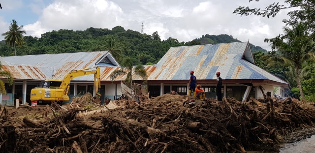 Ekskavator dikerahkan untuk membersihkan sisa-sisa material banjir di halaman SMPN 2 Kalukku, Kabupaten Mamuju. Foto: Sapriadi/SulbarKini