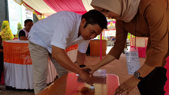 Seorang warga dibantu petugas KPPS untuk mencelupkan tinta setelah melakukan pencoblosan dalam simulasi Pemilu 2019 yang digelar KPU Provinsi Gorontalo, Mingu (03/3). Foto : Burhan Undu