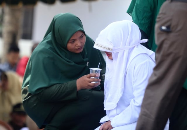 Salah seorang perempuan terhukum cambuk meminta berhenti sebentar saat dieksekusi, petugas memberinya minum di halaman Masjid Syuhada Lamgugob, Banda Aceh, Senin (4/3). Foto: Suparta/acehkini