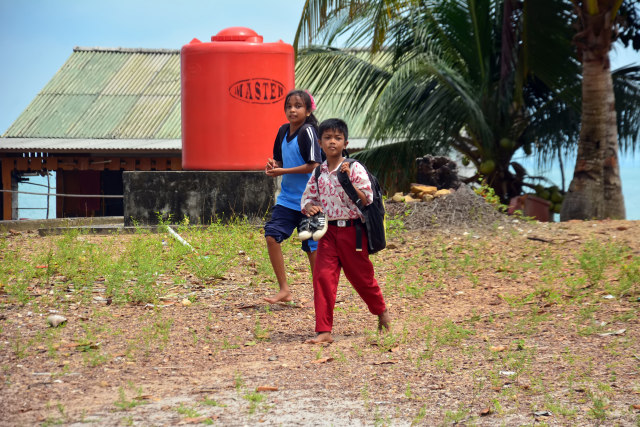 Mereka melepas sepatu bukan karena kebanjiran, tapi karena takut basah terkena percikan ombak saat menyeberangi lautan sepulang dari sekolah. / F. Nurjali