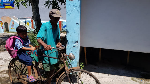 Cindy dibonceng kakeknya, Cokro Utomo Parimin, saat berangkat ke sekolah dengan sepeda onthel. Mereka harus menempuh jarak 2 kilometer setiap hari. Foto: Tugu Jogja/ Galih Wijaya