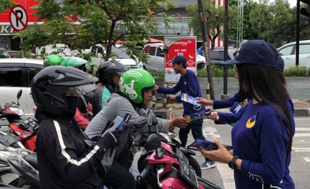 Sejumlah Relawan Partai NasDem Jatim membagikan brosur dan topi di salah satu titik traffic light di Surabaya, Minggu (24/3/2019)