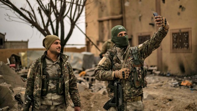 Dua orang Tentara Demokratik Suriah (SDF) melakukan "selfie" di Baghouz, Suriah, setelah ISIS berhasil ditaklukan. Foto: AFP/Delil souleiman