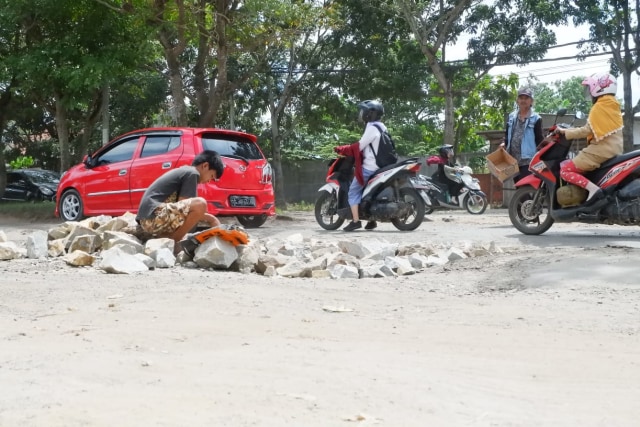 Warga Korpri Raya, Kecamatan Sukarame, Kota Bandar Lampung yang sedang menimbun Jalan Ryacudu dengan batu, Selasa (2/4) | Foto : Obbie Fernando/Lampung Geh