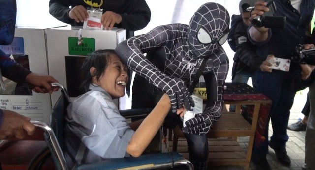 Black Spiderman membantu pemilih disabilitas yang telah selesai mencoblos di TPS 005 Babat Jerawat, Surabaya. Foto : Ridwan Dwi