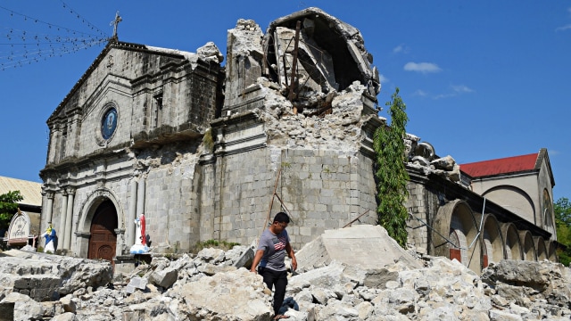 Seorang pekerja gereja berjalan di dekat gereja yang runtuh akibat gempa di Filipina. Foto: AFP/TED ALJIBE