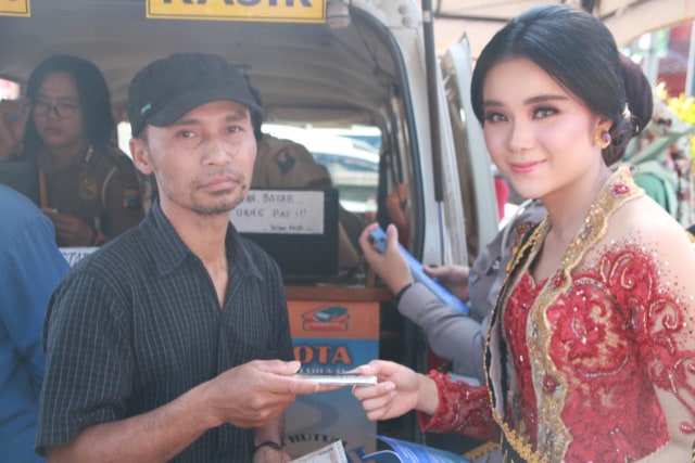 Salah seorang polisi wanita (kanan) dari Polres Malang Kota melayani pembayaran pajak kendaraan bermotor dengan menggunakan kebaya, Rabu (24/4). (foto: Humas Polres Malang Kota).