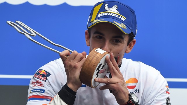 Marc Marquez mencium trofi di atas podium Sirkuit Le Mans sebagai pemenang GP Prancis 2019. Foto: JEAN-FRANCOIS MONIER/AFP