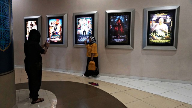 Pengunjung berfoto di depan poster film yang tayang di bioskop. Foto: Iqbal Firdaus/kumparan