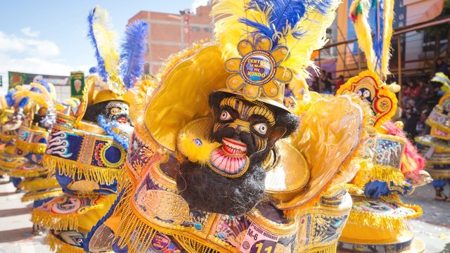 Salah seorang penari berpakaian kuning cerah mengenakan kostum dan topeng dalam karnaval Foto: Shutter Stock