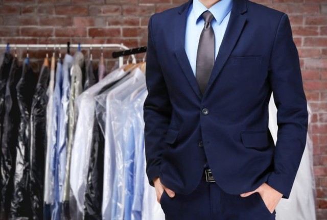 pria memakai jas dengan pakaian dry cleaning digantung