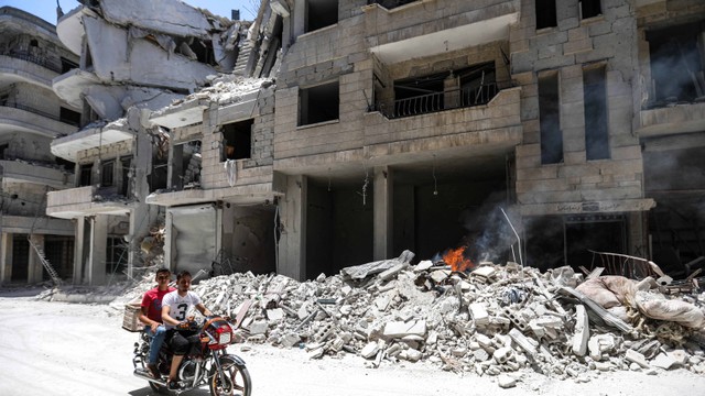 Seorang pengendara motor melintasi depan rumah sakit yang rusak setelah serangan udara di Jisr al-Shughur di provinsi timur laut Suriah Idlib, Rabu (10/7). Foto: AFP/Omar HAJ KADOUR