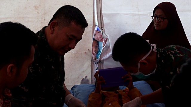 Sejumlah keluarga mengintip dari balik tenda saat proses khitanan massal di Lapangan Merdeka, Balikpapan, Selasa (23/7). Foto: Fanny Kusumawardhani/kumparan