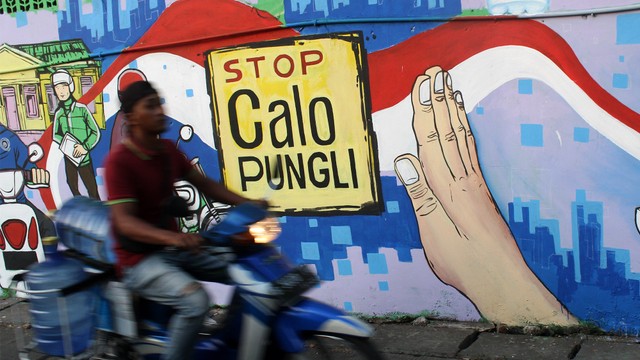 Warga melintas di dekat dinding lukisan mural bertuliskan imbauan stop calo pungutan liar. Foto: ANTARA FOTO/Risky Andrianto