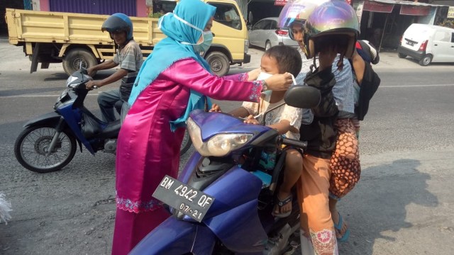 SEORANG pegawai Dinas Kesehatan Provinsi Riau memasangkan masker ke anak-anak. 