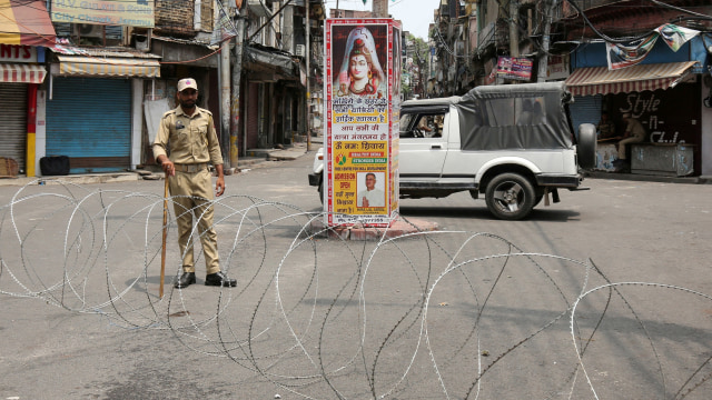 Seorang petugas keamanan India berjaga di sepanjang jalan yang sepi selama pembatasan di Jammu. Foto: REUTERS/Mukesh Gupta