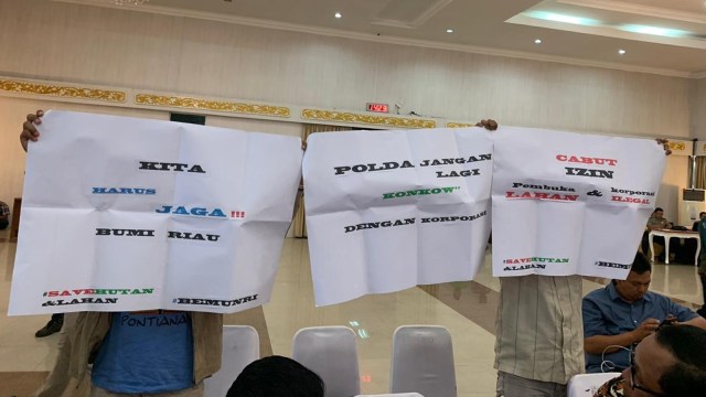 DUA mahasiswa Universitas Riau membentangkan karton bertuliskan kritikan saat Kapolda Riau Irjen Pol Widodo Eko Prihastopo sedang pidato bahas Karhutla, Kamis, 8 Agustus 2019, di Gedung Daerah Riau. 