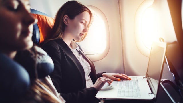 Ilustrasi penumpang wanita duduk di bangku tengah pesawat sambil bekerja Foto: Shutter Stock