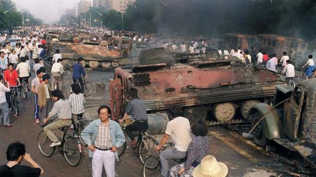 Warga Beijing berada di dekat kendaraan taktis yang dibakar oleh demonstran untuk mencegah pasukan bergerak ke Lapangan Tiananmen pada 4 Juni 1989. Foto: AFP/MANUEL CENETA