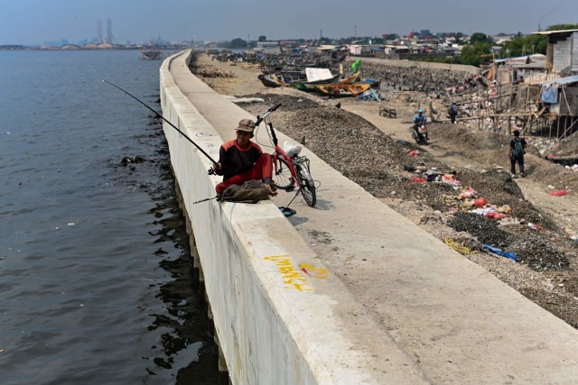 Seorang pria memancing dari atas tembok laut raksasa di Jakarta Utara. Foto: AFP/BAY ISMOYO