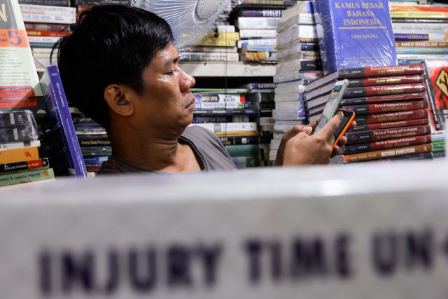 Darussalam melayani pembeli buku lewat gadgetnya di sentra buku Kwitang, Jakarta Pusat. Foto: Jamal Ramadhan/kumparan