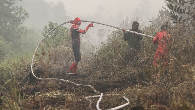 Seorang warga mengenakan kostum superhero membantu memadamkan kebakaran lahan gambut di Rimbo Panjang, Kabupaten Kampar, Riau, Kamis (12/9/2019). Foto: ANTARA FOTO/Iggoy el Fitra