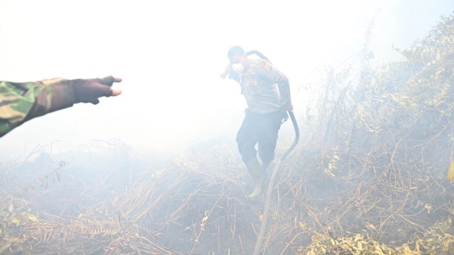 Petugas pemadam kebakaran menyemprotkan air untuk membantu memadamkan api di Kampar, Provinsi Riau. Foto: AFP/ADEK BERRY