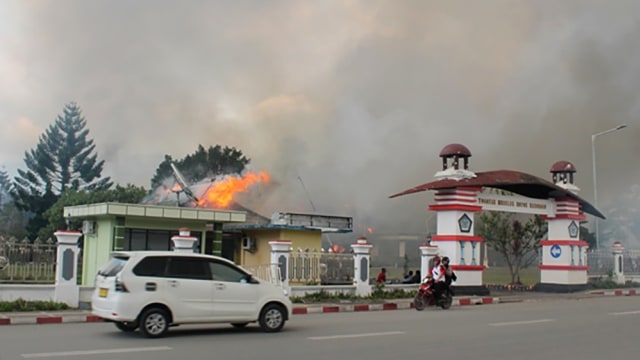 Pengendara melintasi Kantor Bupati Jayawijaya yang terbakar saat aksi unjuk rasa di Wamena, Jayawijaya, Papua, Senin (23/9/2019). Foto: ANTARA FOTO/Marius Wonyewun