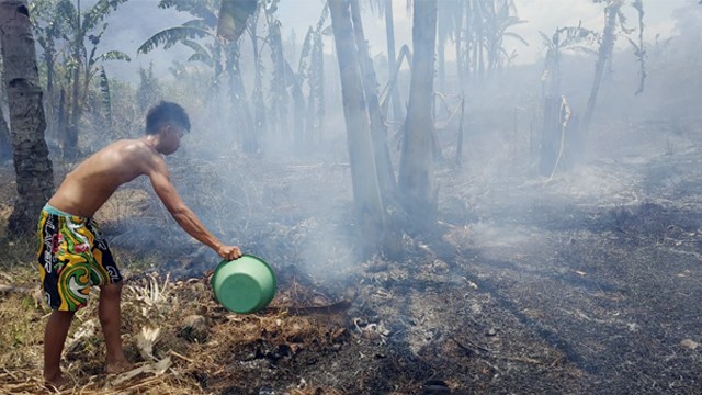 Seorang warga menggunakan baskom air untuk memadamkan api yang membakar lahan di Desa Solimandungan, Kecamatan Bolaang, Kabupaten Bolaang Mongondow, Sulawesi Utara.