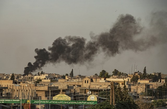 Kepulan asap terlihat dari salah satu bangunan di kota Ras al Ain, Suriah saat Turki melakukan serangan ke kota tersebut, Rabu,(9/10/2019). Foto: AFP/DELIL SOULEIMAN