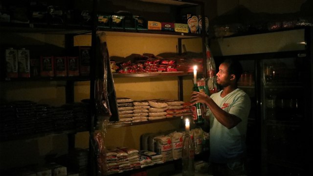 Seorang pedagang menyalakan lilin untuk menerangi ruangan saat listrik padam. Foto: REUTERS/Siphiwe Sibeko