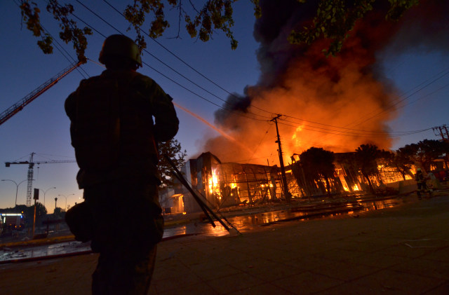 Seorang tentara berjaga disekitar bangunan yang dibakar demonstran di Concepcion, Chile, Senin (21/10/2019). Foto: AFP/GUILLERMO SALGADO