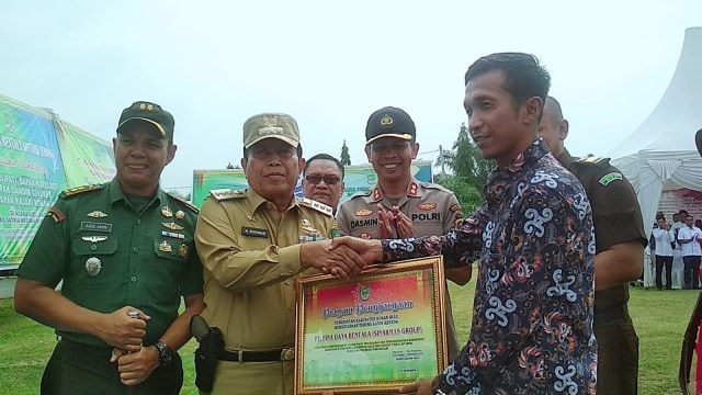 BUPATI Rokan Hulu, Riau, Sukiman, menyerahkan penghargaan kepada warga, Rabu, (6/11/2019). Di pinggangnya terselip pistol, diduga air softgun.
