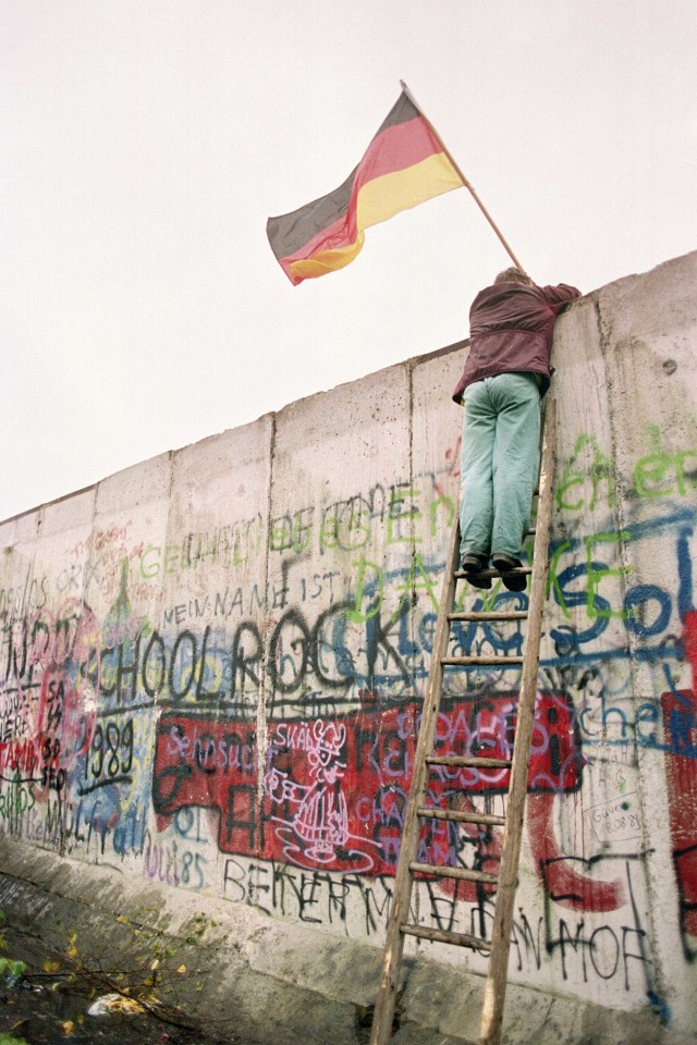 Warga Jerman Barat memegang bendera Jerman Barat kepada polisi Jerman Timur pada 11 November 1989. Foto: AFP/PATRICK HERTZOG