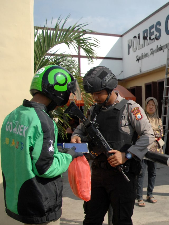 Petugas kepolisian memeriksa barang pengemudi ojek online yang akan masuk mengantar pesanan di Polres Kabupaten Gowa, Sulawesi Selatan, Rabu (13/11/2019).  Foto:  ANTARA FOTO/Abriawan Abhe